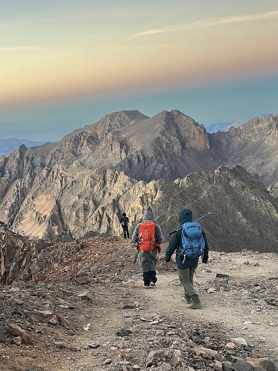 Hiker's boots and backpack on a rocky High Atlas trail with mountain panorama beyond